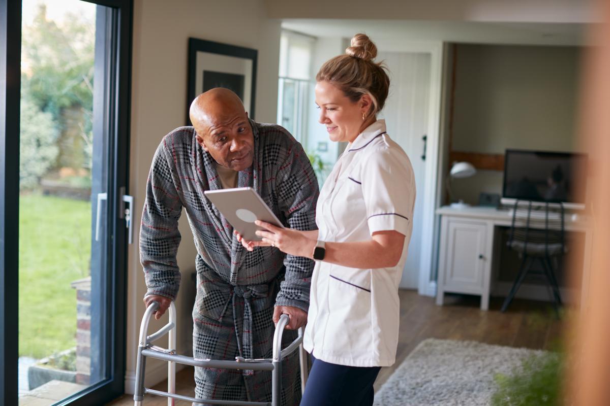 Verpleegster in gesprek met oude man met rolator
