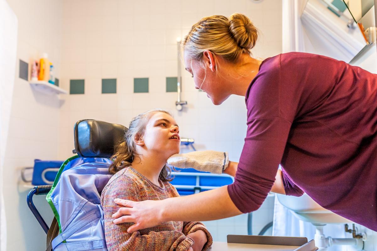 meisje met verstandelijke en lichamelijke beperking in rolstoel met verzorgendev
