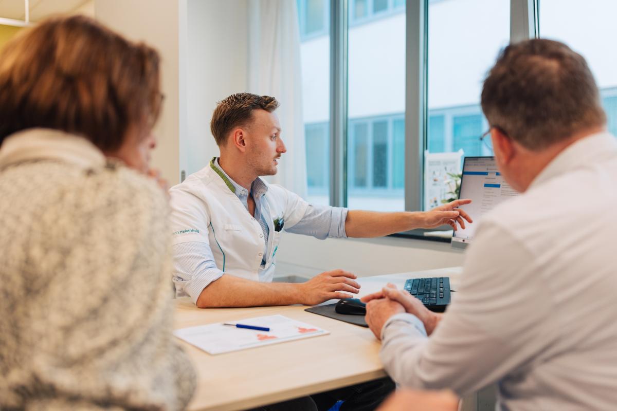 arts voer proactieve zorgplanningsgesprek met patiënt en naaste aan zijn bureau in het ziekenhuis